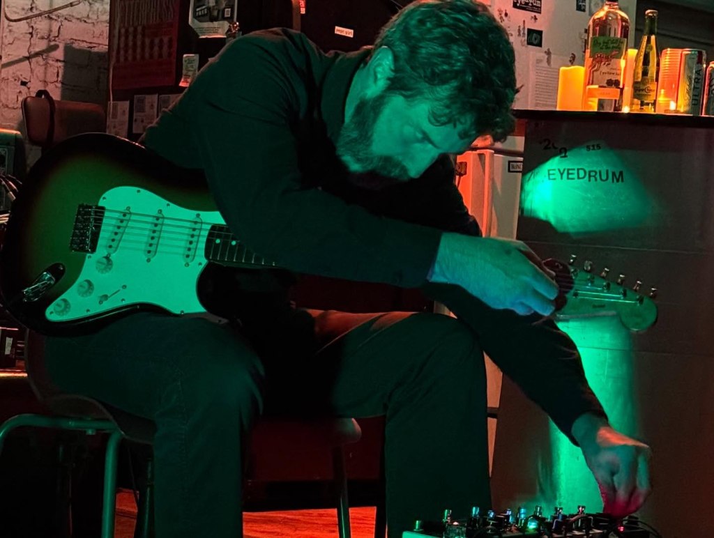 Colin Bragg playing a Stratocaster while twisting an effect pedal knob.
