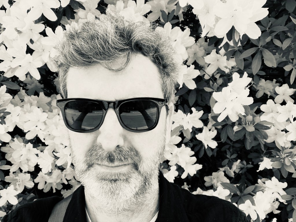 Colin with Ray Bans in front of a giant azalea bush