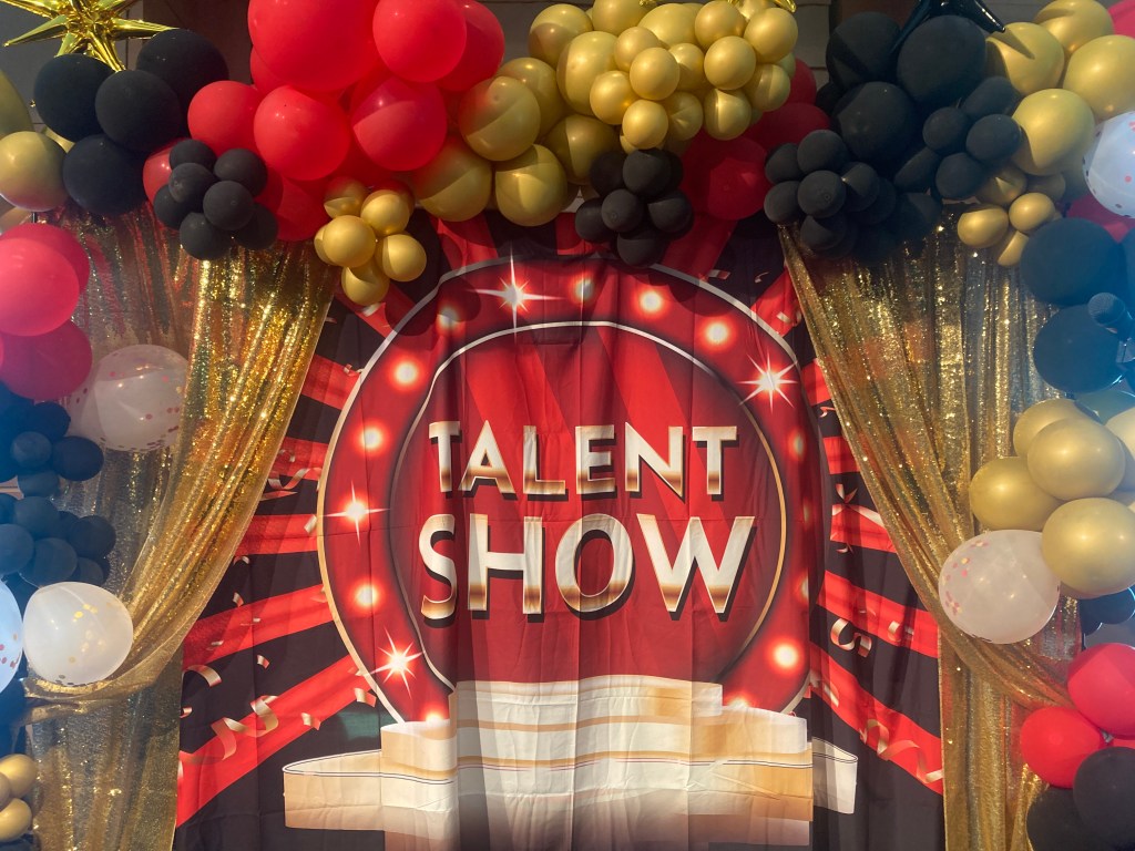 talent show backdrop, with small balloons draped around a graphic screen like grapes