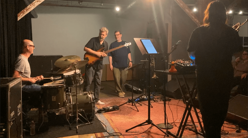Members a jazz combo converse and laugh between numbers at a gallery show.